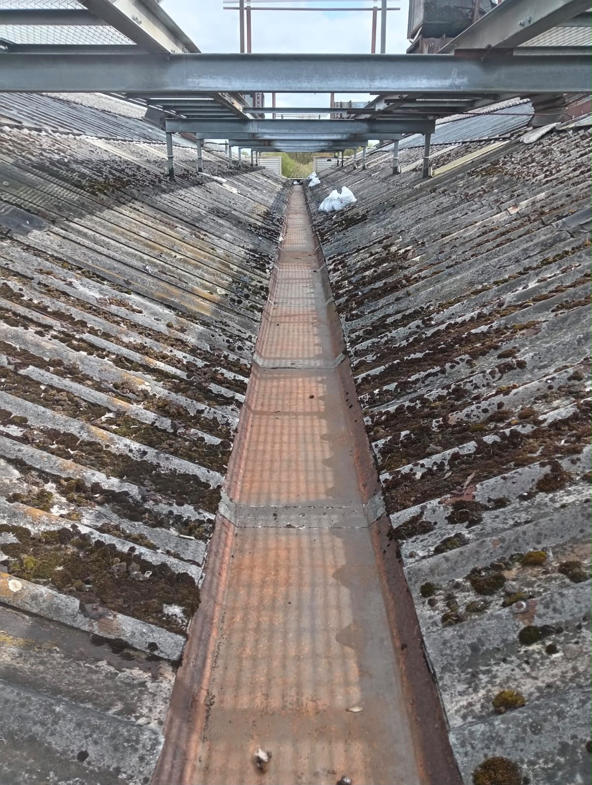 Rusted metal valley gutter between industrial roof slopes prior to replacement