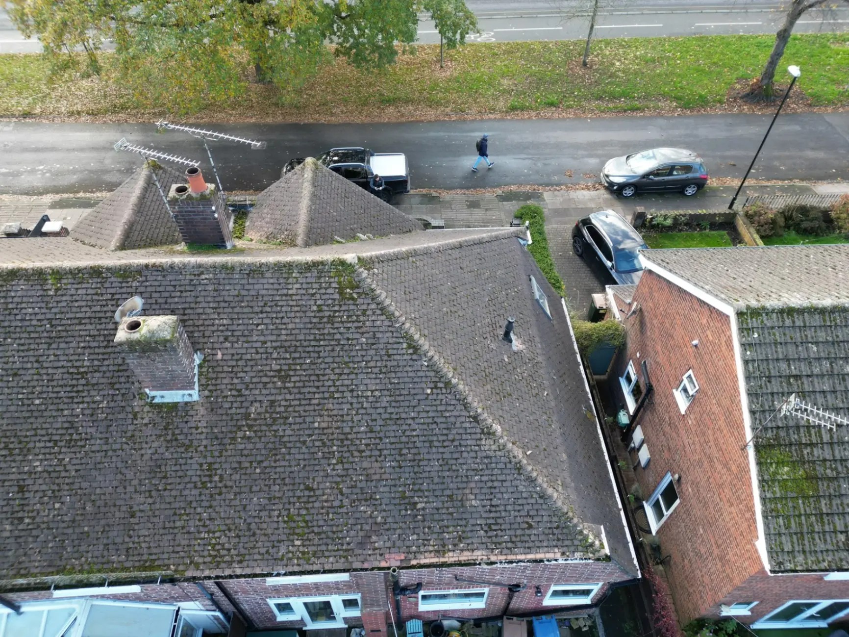 Aerial view of a tired moss-covered tiled roof with old chimney and worn hips on a Coventry semi-detached house before re-roofing